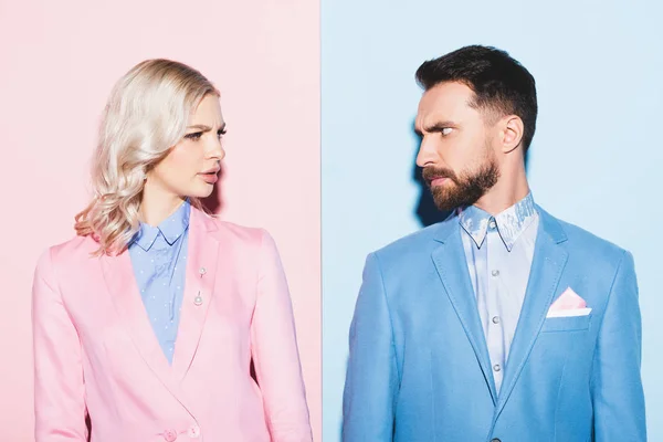 Irritated woman and handsome man looking at each other on pink and blue background — Stock Photo