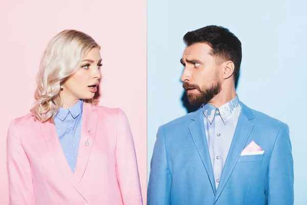 Schockierte Frau und gutaussehender Mann schauen einander auf rosa und blauem Hintergrund an — Stockfoto