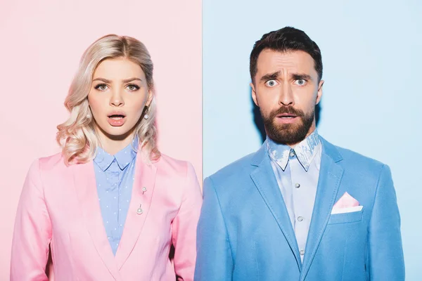 Shocked woman and handsome man looking at camera on pink and blue background — Stock Photo