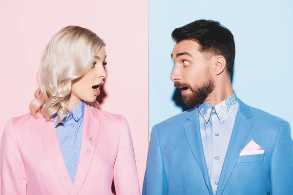 Shocked woman and handsome man looking at each other on pink and blue background — Stock Photo