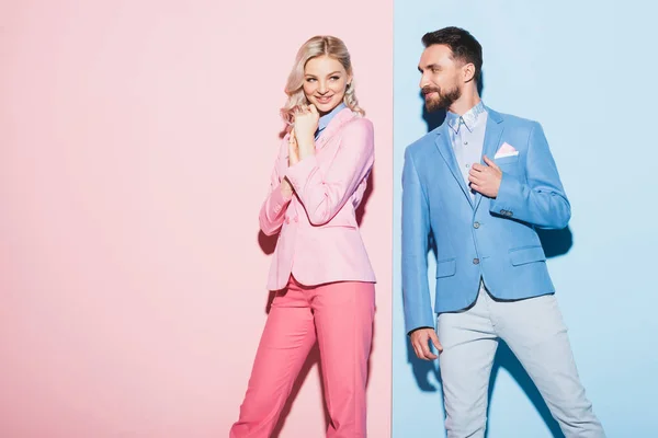 Attraktive Frau und lächelnder Mann, der sie auf rosa und blauem Hintergrund ansieht — Stockfoto