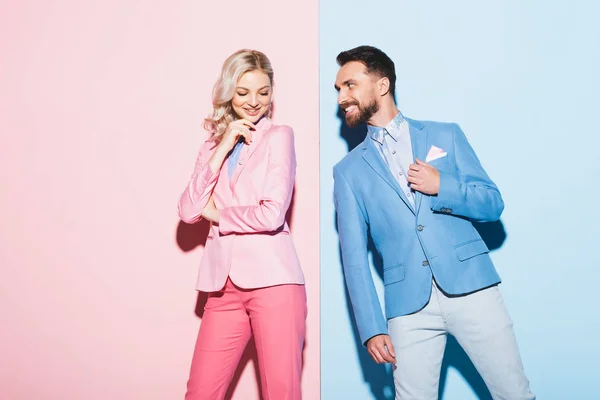 Mujer atractiva y hombre sonriente mirándola sobre fondo rosa y azul - foto de stock