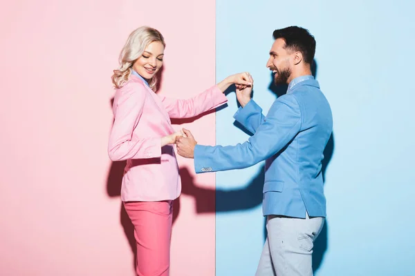 Smiling woman and handsome man holding hands on pink and blue background — Stock Photo
