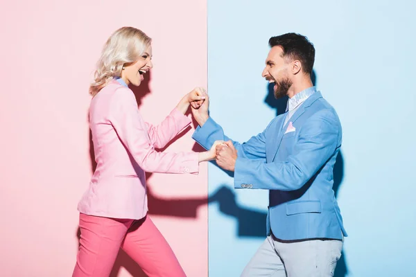 Vista lateral de la mujer sonriente y el hombre guapo cogido de la mano sobre fondo rosa y azul - foto de stock