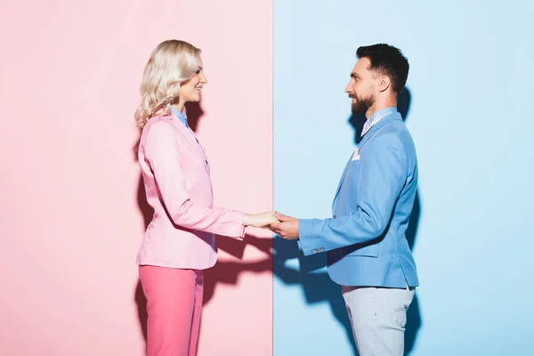 Вид сбоку улыбающейся женщины и красивого мужчины, держащегося за руки на розовом и голубом фоне — стоковое фото