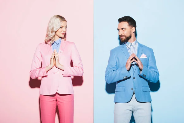 Atractiva mujer y hombre sonriente con las manos de oración sobre fondo rosa y azul - foto de stock