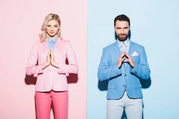 Mulher atraente e homem sorridente com as mãos de oração sobre fundo rosa e azul — Fotografia de Stock