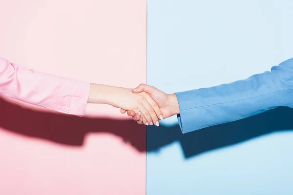 Vista recortada de la mujer y el hombre estrechando las manos sobre fondo rosa y azul - foto de stock