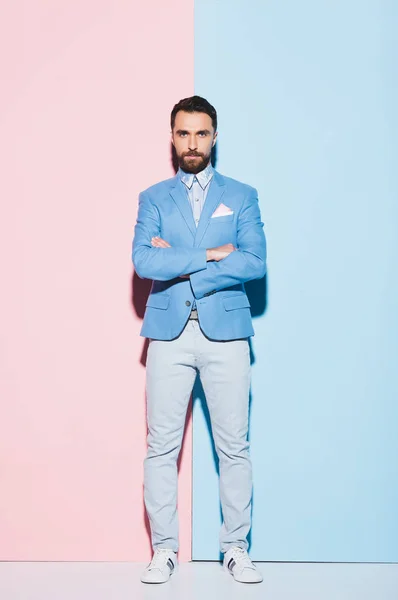 Serious man with crossed arms looking at camera on pink and blue background — Stock Photo