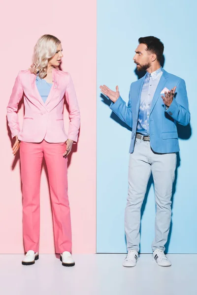 Angry woman and handsome man quarreling on pink and blue background — Stock Photo