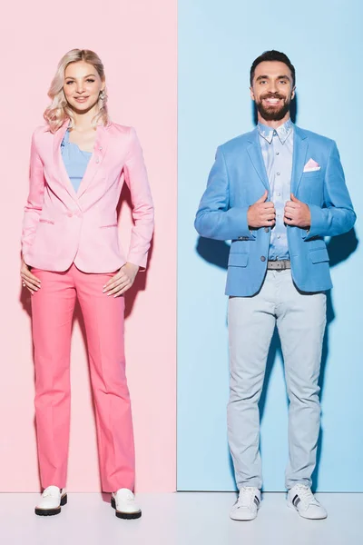 Lächelnde Frau und gutaussehender Mann, der in die Kamera auf rosa und blauem Hintergrund blickt — Stockfoto
