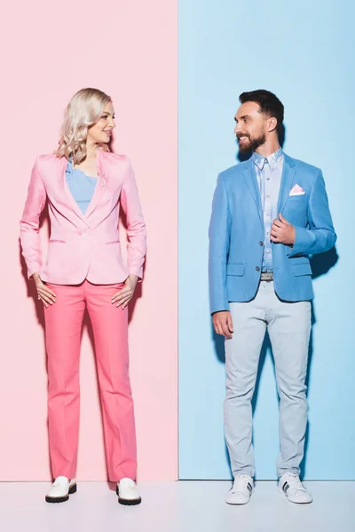 Smiling woman and handsome man looking at each other on pink and blue background — Stock Photo