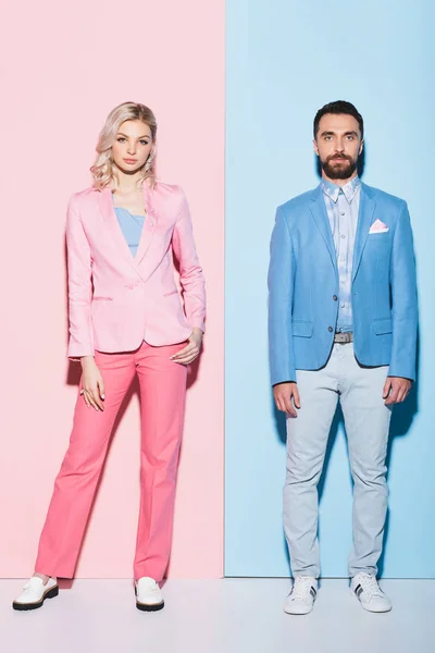 Attraktive Frau und gutaussehender Mann schaut in die Kamera auf rosa und blauem Hintergrund — Stockfoto
