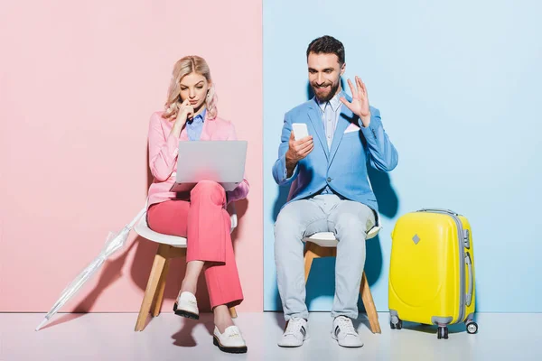 Woman using laptop and smiling man having video call on pink and blue background — Stock Photo