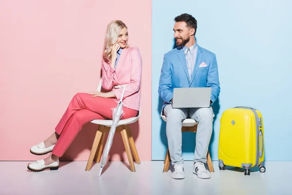 Mujer sonriente hablando en el teléfono inteligente y hombre guapo con ordenador portátil sobre fondo rosa y azul - foto de stock