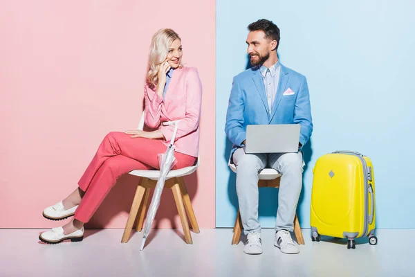 Mujer sonriente hablando en el teléfono inteligente y hombre guapo con ordenador portátil sobre fondo rosa y azul - foto de stock