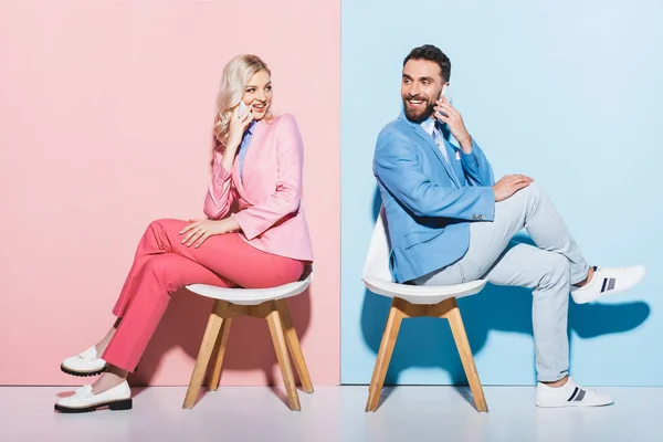 Smiling woman and handsome man talking on smartphones on pink and blue background — Stock Photo