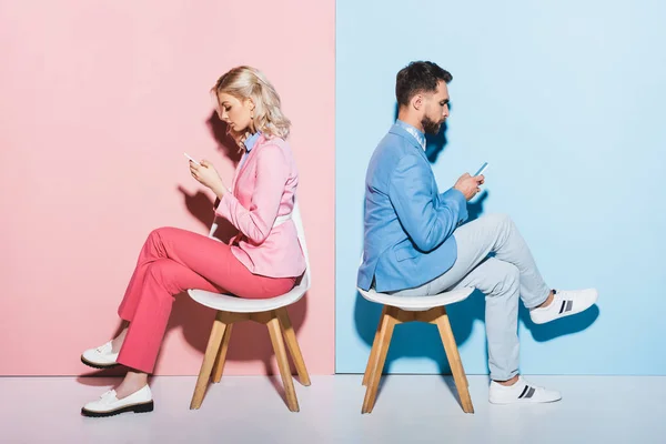 Side view of woman and handsome man using smartphones on pink and blue background — Stock Photo