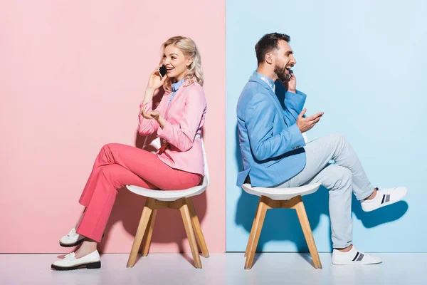 Smiling woman and handsome man talking on smartphones on pink and blue background — Stock Photo