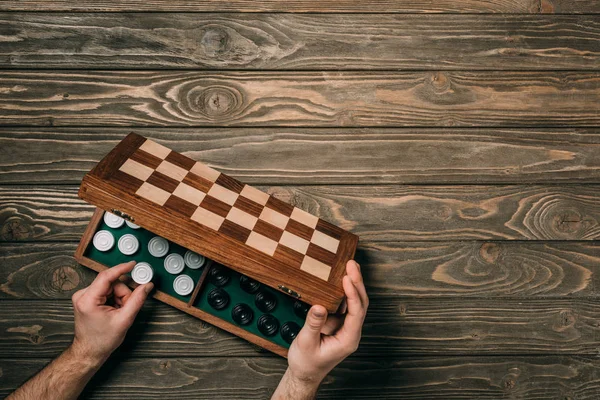 Cropped view of man taking checker from checkerboard on wooden background — Stock Photo