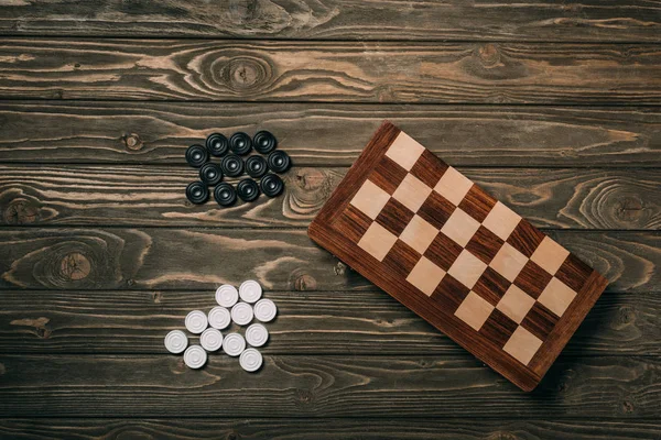 Top view of checkers beside chessboard on wooden background — Stock Photo