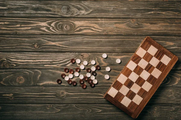 Top view of checkers and checkerboard on textured wooden surface — Stock Photo