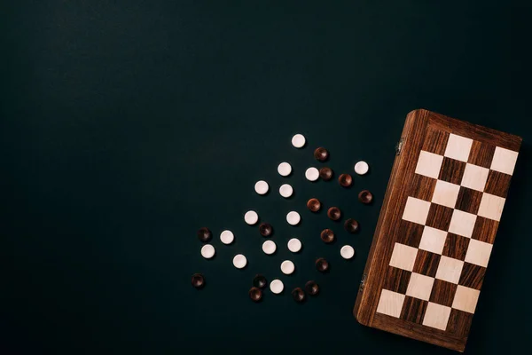 Вид зверху на біло-коричневі шашки з шахівницею ізольовані на чорному — стокове фото