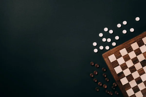 Top view of checkers by checkerboard isolated on black with copy space — Stock Photo