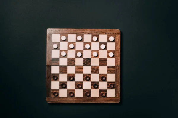 Top view of checkers on wooden checkerboard isolated on black — Stock Photo