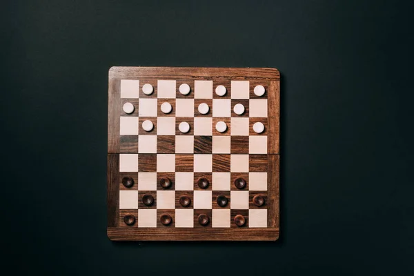 Vue du dessus des dames sur damier en bois isolé sur noir — Photo de stock