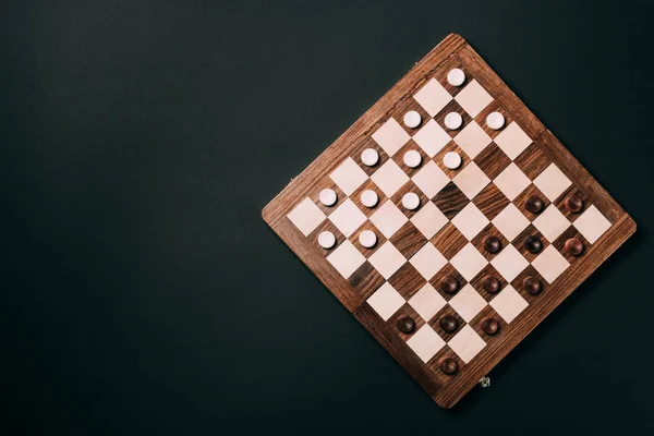 Top view of wooden checkerboard with checkers isolated on black — Stock Photo