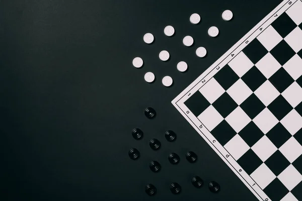 Top view of black and white checkers and checkerboard isolated on black — Stock Photo