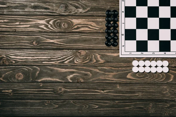 Top view of checkers beside checkerboard on wooden background with copy space — Stock Photo