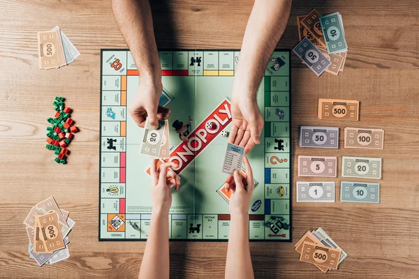 KYIV, UKRAINE - NOVEMBER 15, 2019: Cropped view of man and woman playing monopoly game at table — Stock Photo