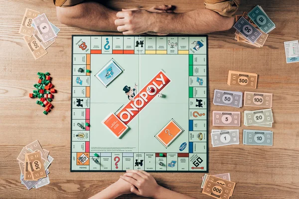 KYIV, UKRAINE - NOVEMBER 15, 2019: Top view of man and woman playing monopoly at wooden table — Stock Photo