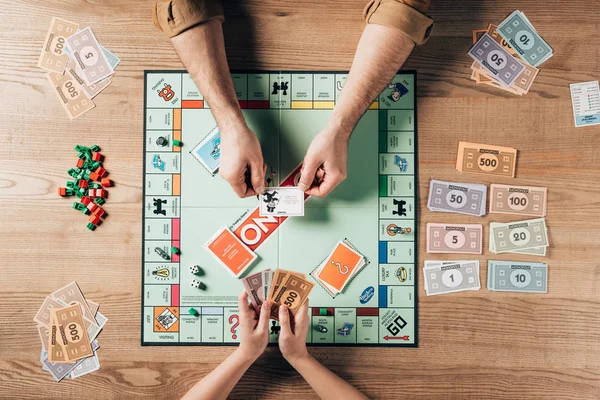 KYIV, UKRAINE - NOVEMBER 15, 2019: Cropped view of man holding explanation card and woman with toy currency while playing in monopoly game — Stock Photo