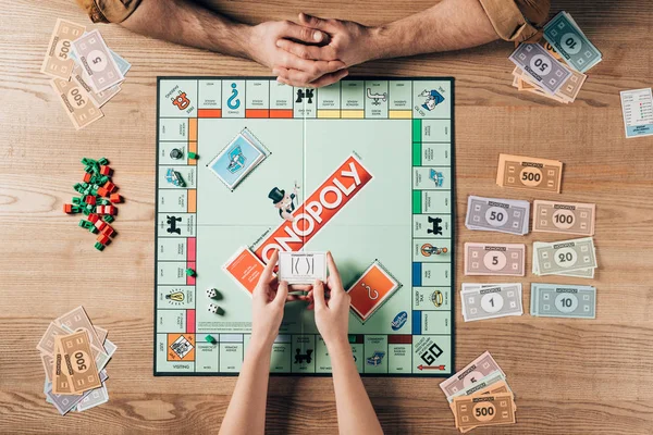 KYIV, UKRAINE - NOVEMBER 15, 2019: Cropped view of woman and man playing monopoly board game at table — Stock Photo