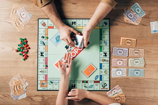 KYIV, UKRAINE - NOVEMBER 15, 2019: Cropped view of woman holding dices and man with explanation cards by monopoly game at table — Stock Photo