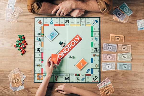 KYIV, UKRAINE - NOVEMBER 15, 2019: Cropped view of woman holding cards while playing with man in monopoly at table — Stock Photo