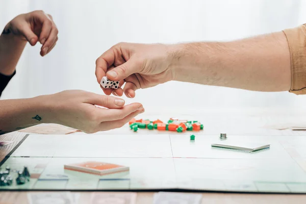 KYIV, UKRAINE - NOVEMBER 15, 2019: Cropped view of man giving to woman playing dices with monopoly game on table — Stock Photo