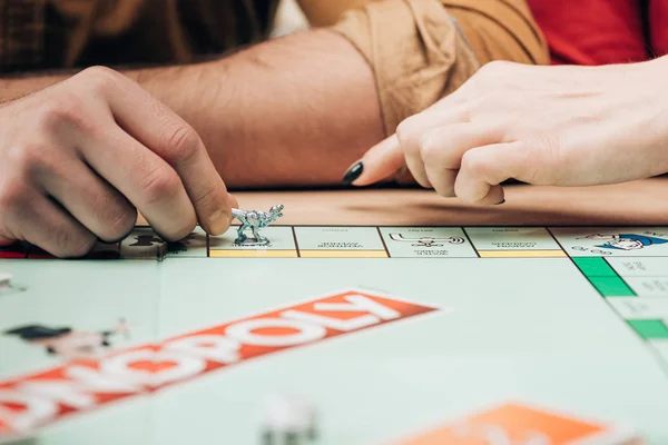 KYIV, UCRANIA - 15 de noviembre de 2019: Vista recortada del hombre y la mujer con figura de juego en el juego de mesa monopolio - foto de stock