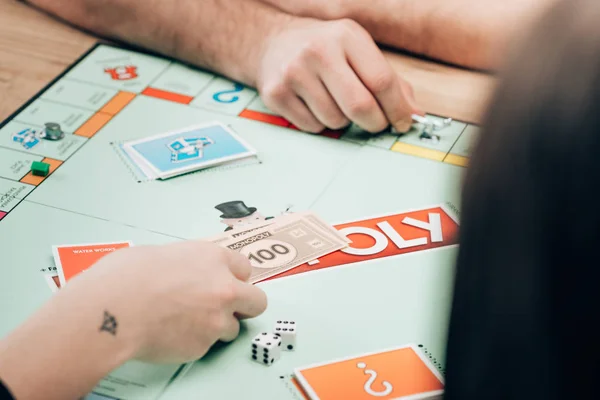 KYIV, UCRANIA - 15 de noviembre de 2019: Vista recortada de hombres y mujeres jugando al juego de mesa monopolista - foto de stock