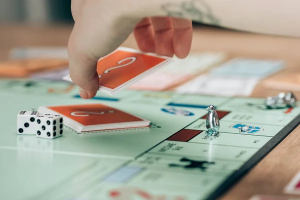 KYIV, UKRAINE - NOVEMBER 15, 2019:Cropped view of woman holding card by dices on monopoly game — Stock Photo