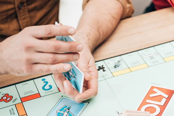 KYIV, UKRAINE - NOVEMBER 15, 2019: Cropped view of man holding cards of monopoly game at table — Stock Photo