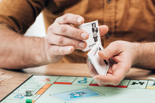 KYIV, UCRAINA - 15 NOVEMBRE 2019: Vista ritagliata dell'uomo in possesso di carte di spiegazione con gioco monopolistico sul tavolo — Foto stock