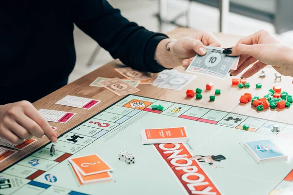 KYIV, UKRAINE - NOVEMBER 15, 2019: Cropped view of women with toy currency playing monopoly at table — Stock Photo