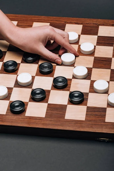 Cropped view of woman holding white checker on checkerboard on black background — Stock Photo