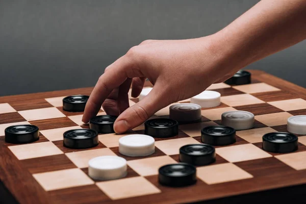 Cropped view of woman holding checker on wooden checkerboard on grey background — Stock Photo