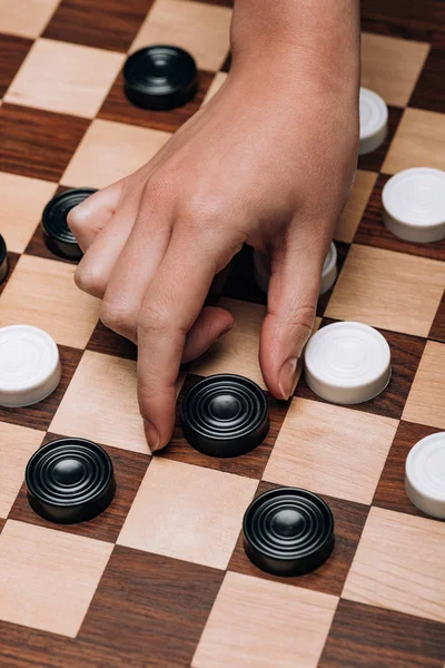 Cropped view of woman holding black checker on wooden checkerboard — Stock Photo