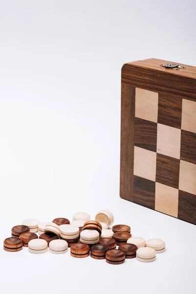 Pile of wooden checkers by checkerboard isolated on white — Stock Photo